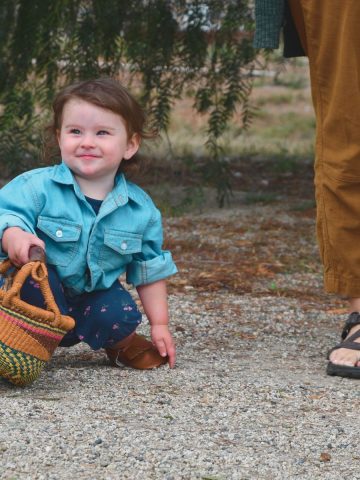 Baby squatting touching shoe holding basket near mom