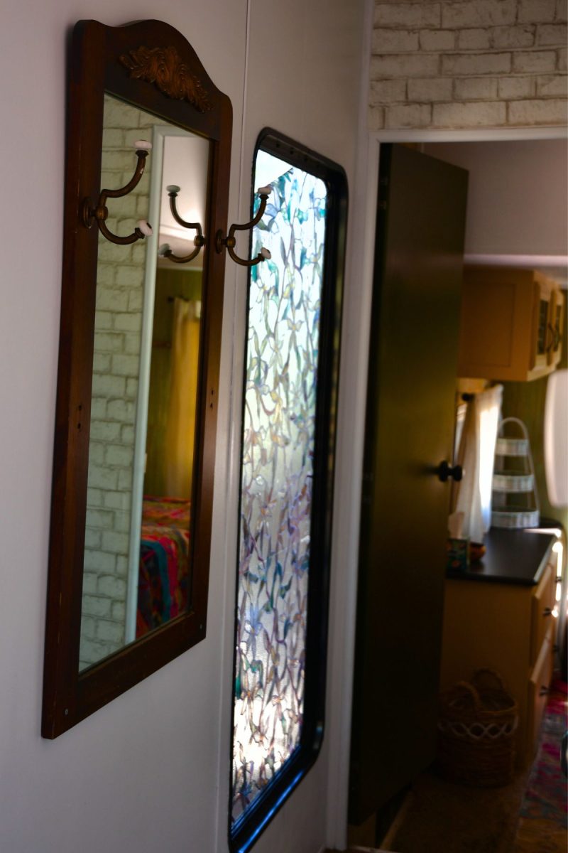 Stained glass style cling on film placed on hall window in travel trailer next to a vintage mirror and coat hooks