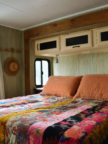 cotton velour comforter multi patterened on queen bed in travel trailer. wall paper and wood stained trim.