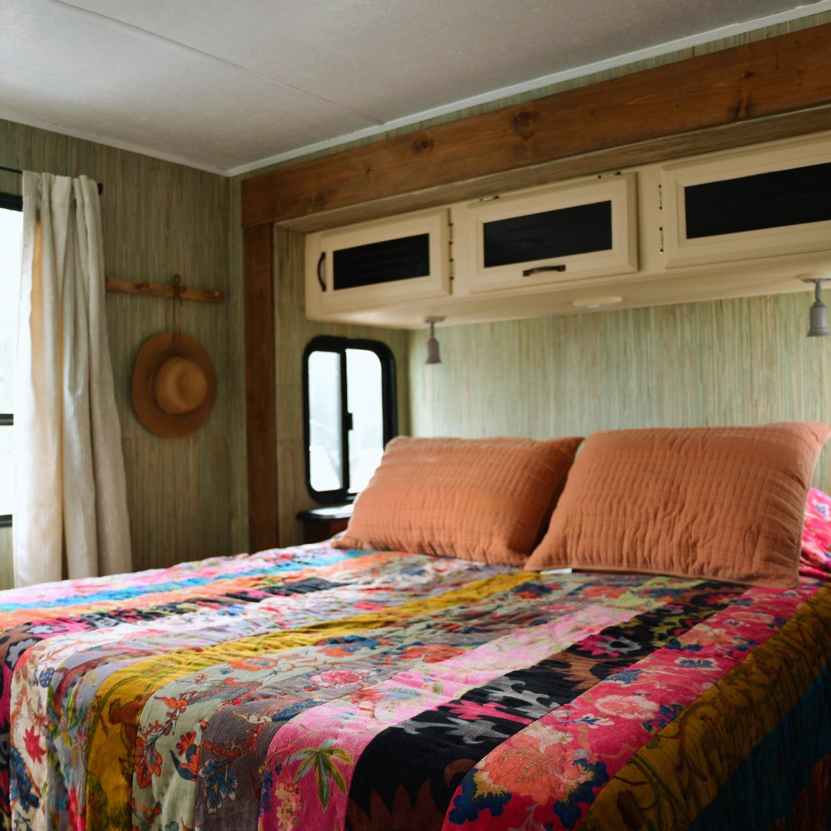 cotton velour comforter multi patterened on queen bed in travel trailer. wall paper and wood stained trim.